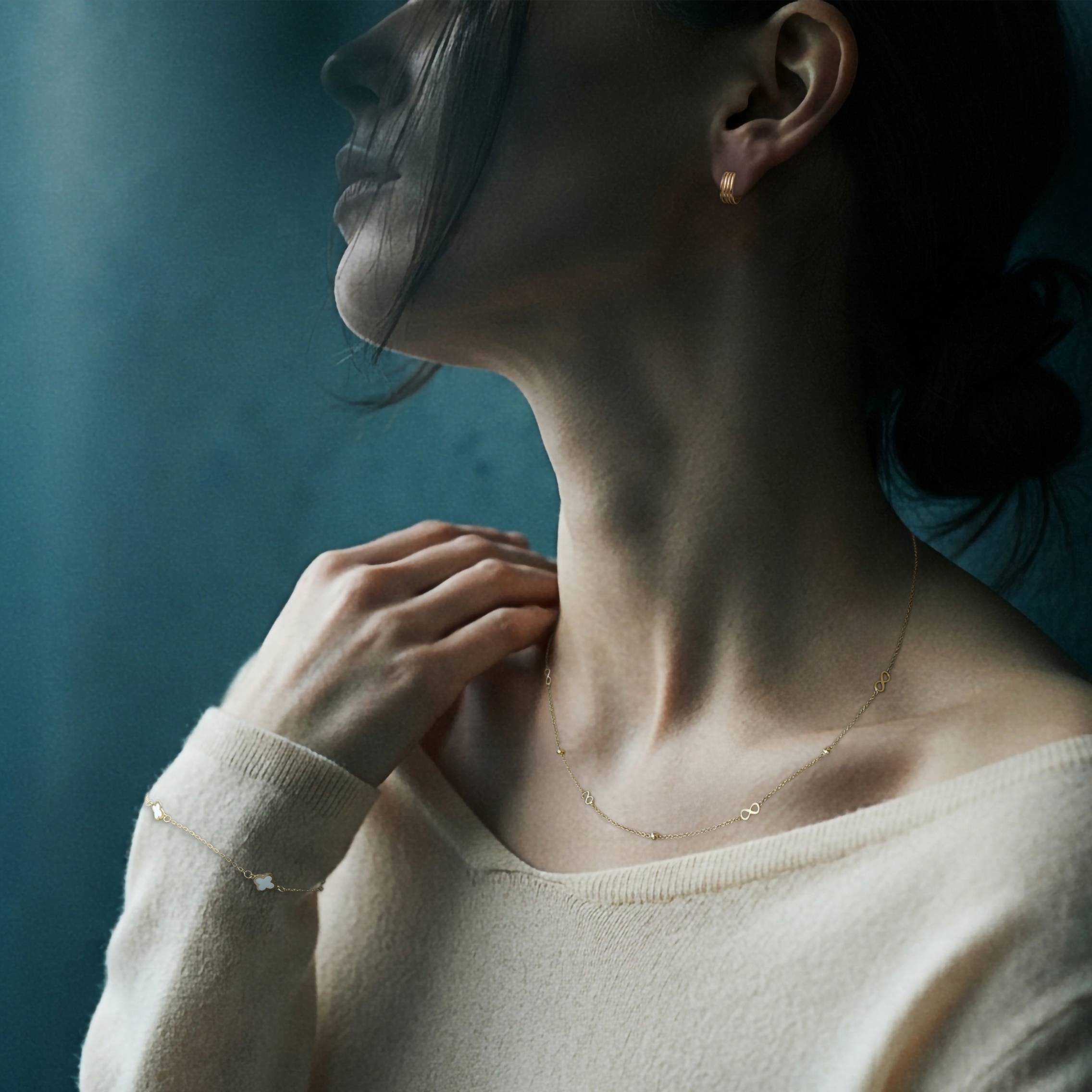 Woman wearing a gold earring, a gold necklace with infinity symbols and a bracelet with clovers from Nordic Bling.