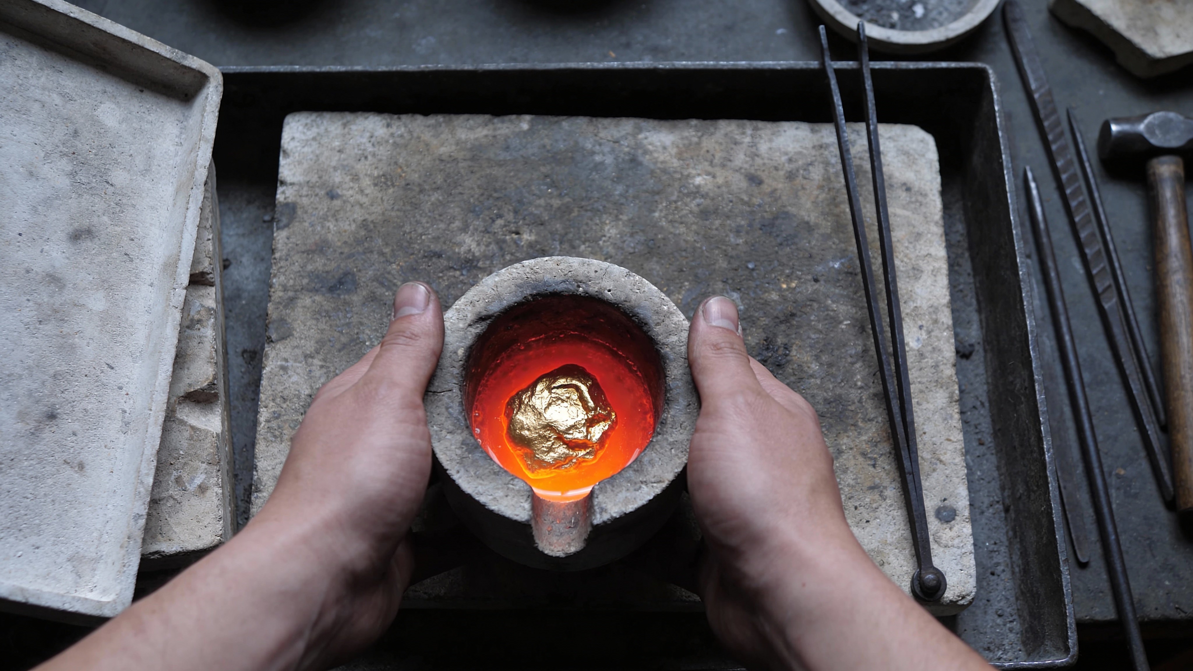 A crucible containing glowing molten gold held by a craftsman.