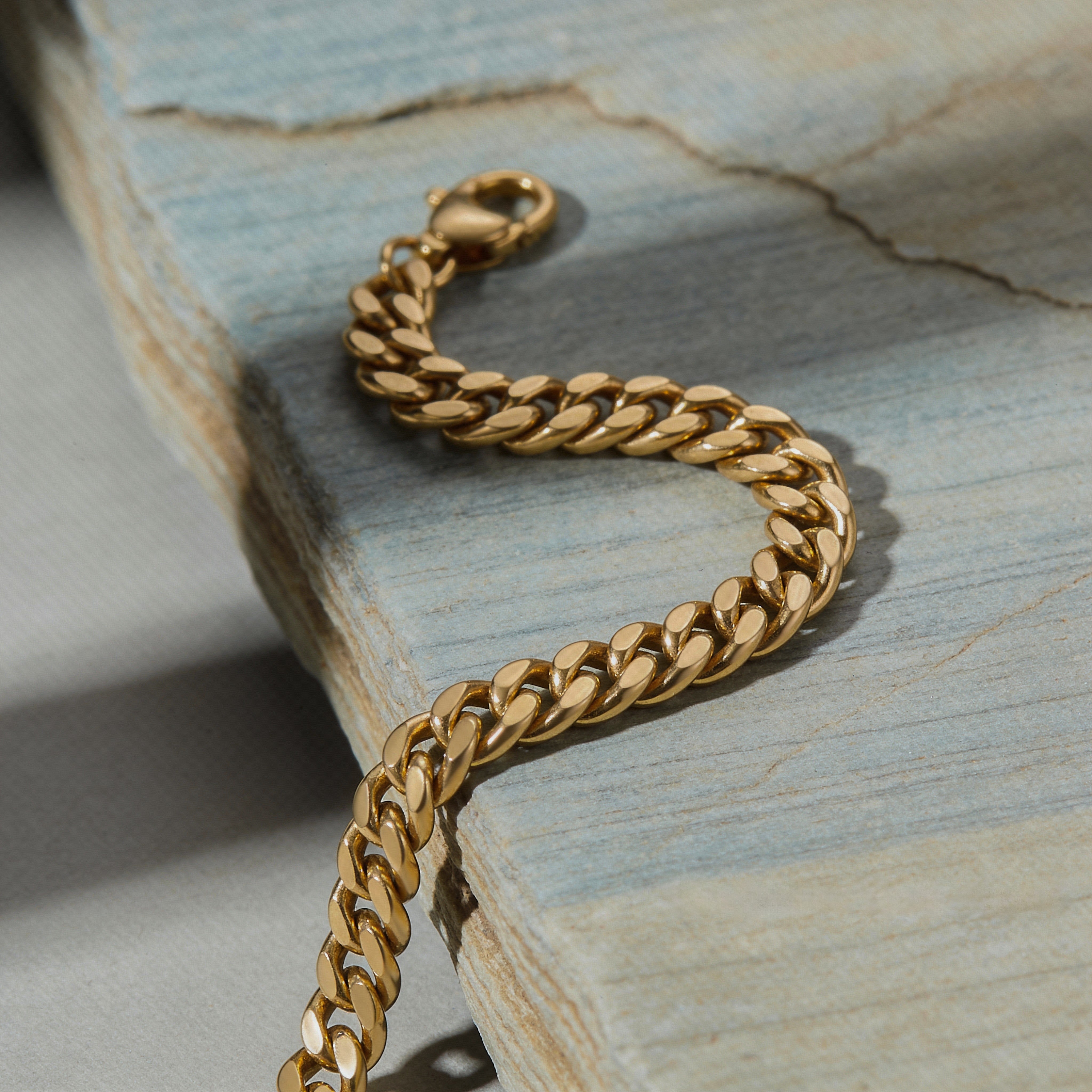 A bold gold curb chain bracelet resting on a natural blue-toned stone surface.