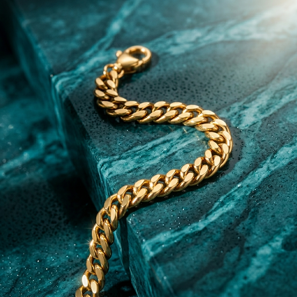 A bold gold curb chain bracelet resting on a natural teal-toned stone surface.